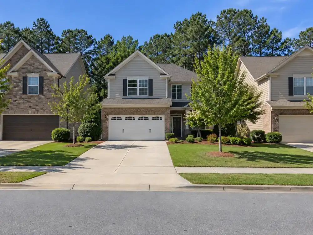 Two-story suburban homes with attached garage doors, green lawns and trees along the sidewalk