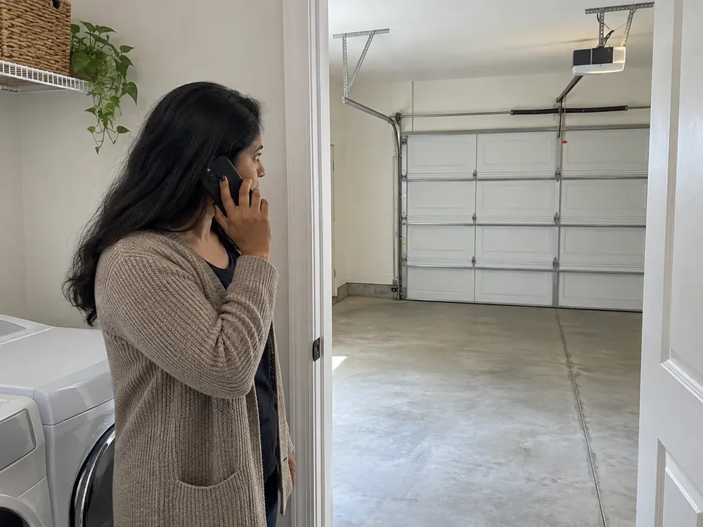 Homeowner speaking on a phone in a laundry doorway facing a closed garage door