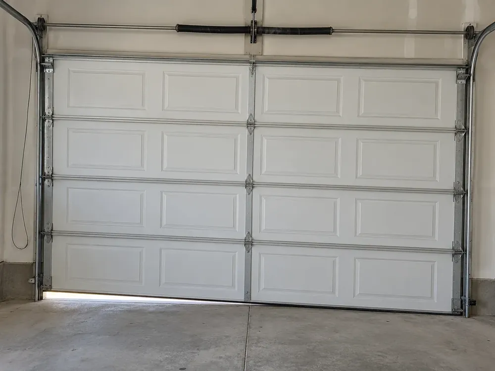 Crooked white garage door with a slack cable loop beside the left track