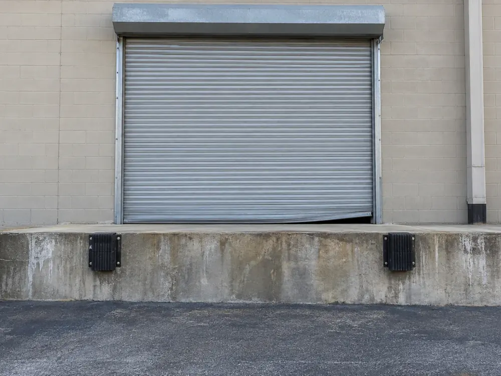Closed rolling steel door with a bent bottom bar above a warehouse loading dock