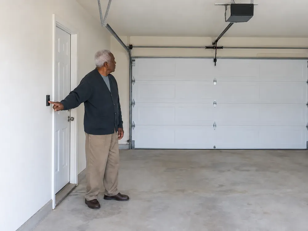 Homeowner pressing a wall control while looking at a closed white garage door.