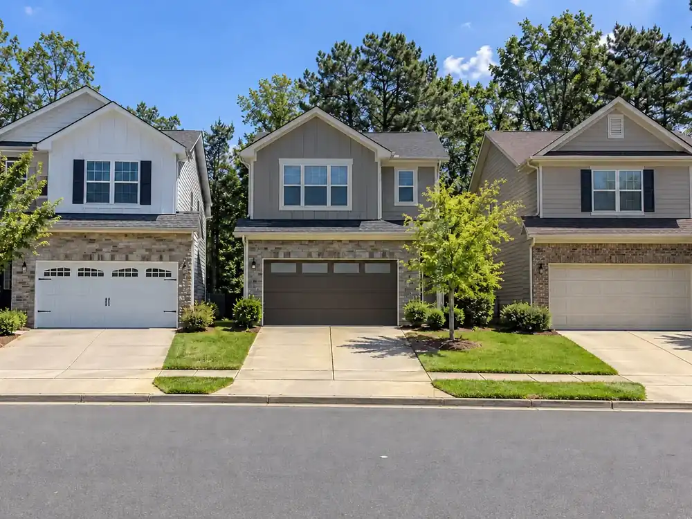 Three neighboring houses with white carriage-house, dark-bronze flat-panel and almond raised-panel garage doors.